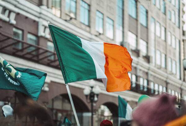 National Flag of Ireland close-up above people crowd, city street, traditional carnival of St. Patrick's Day